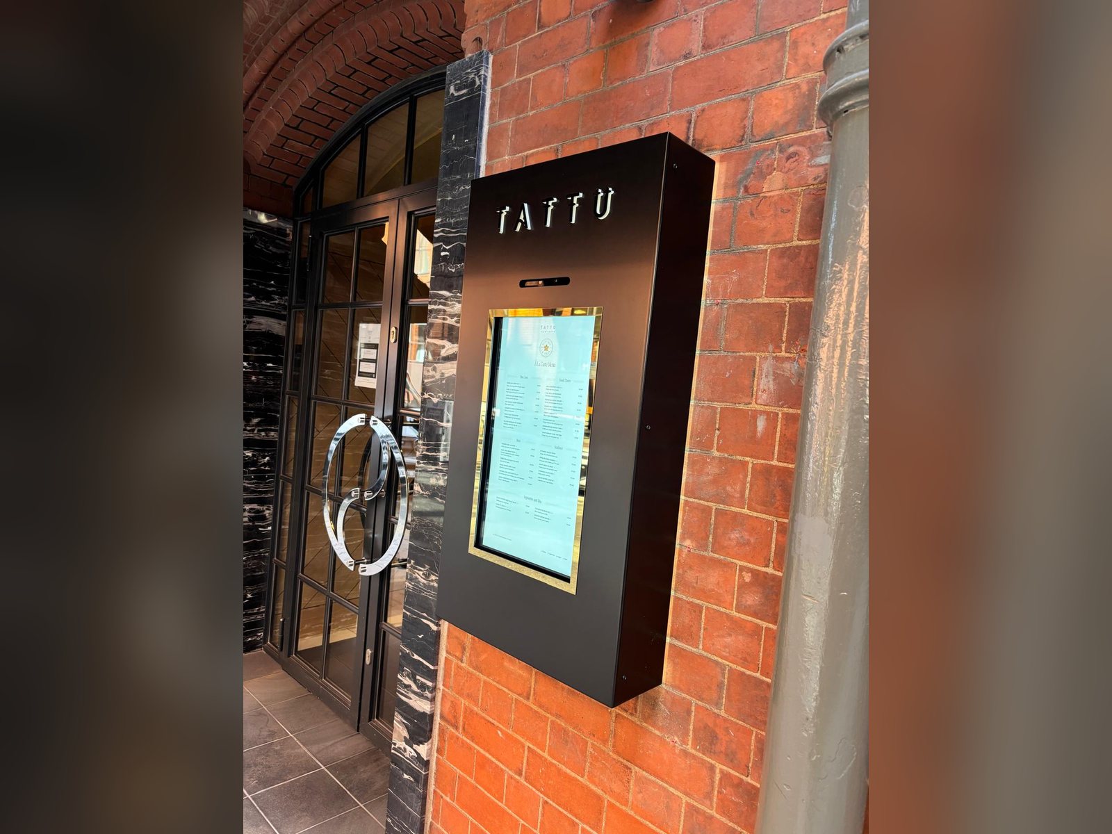 Outdoor digital menu screen in a black branded housing at a Manchester restaurant entrance