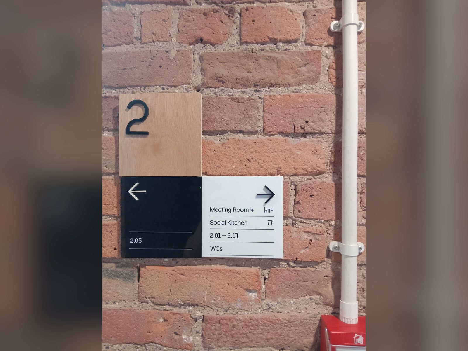 Tactile floor number and directional sign on an exposed brick wall