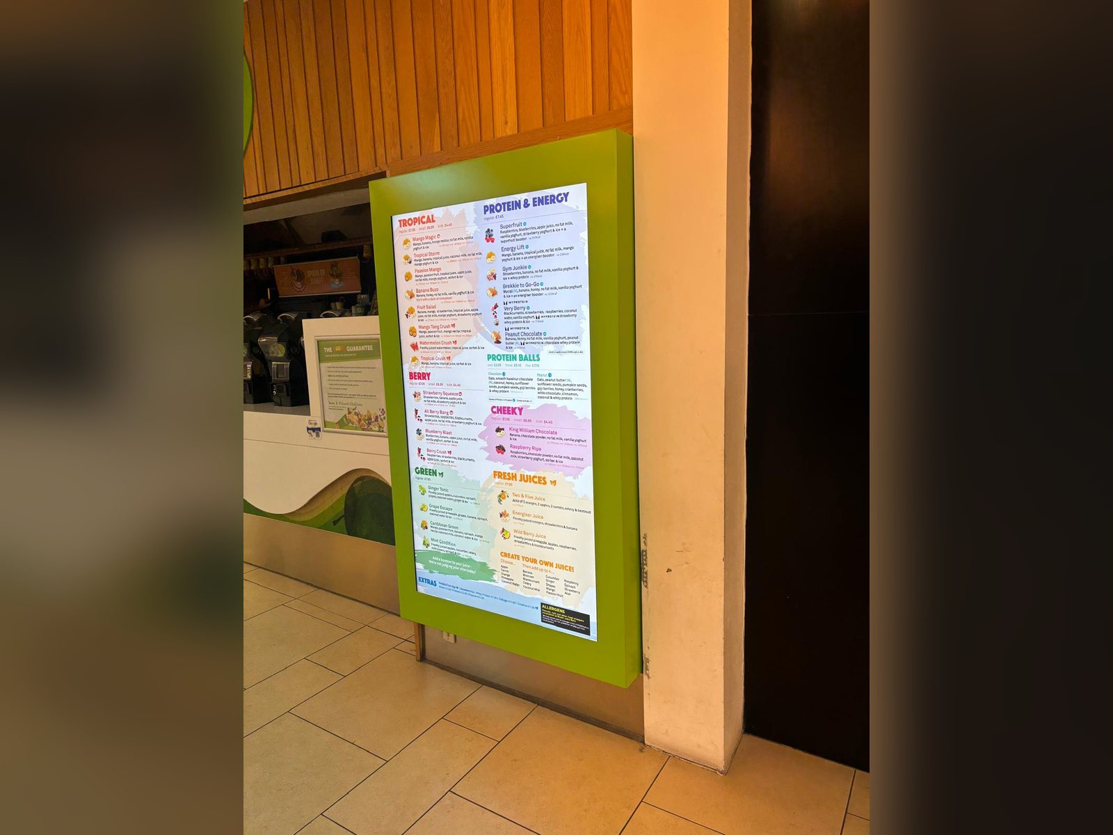 Freestanding digital menu screen in a coloured housing inside a food outlet