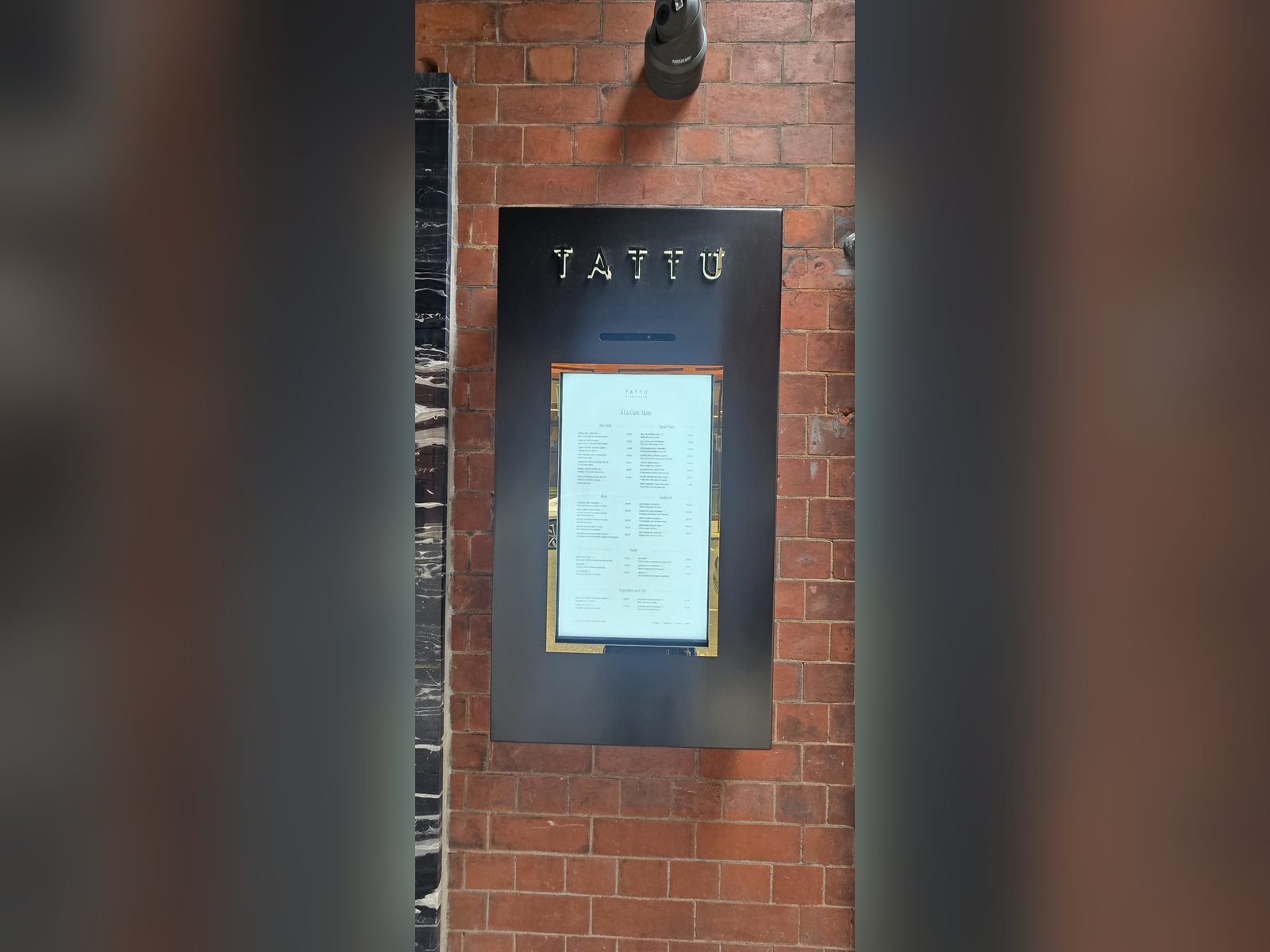 Digital menu screen set in a branded black housing on a brick wall