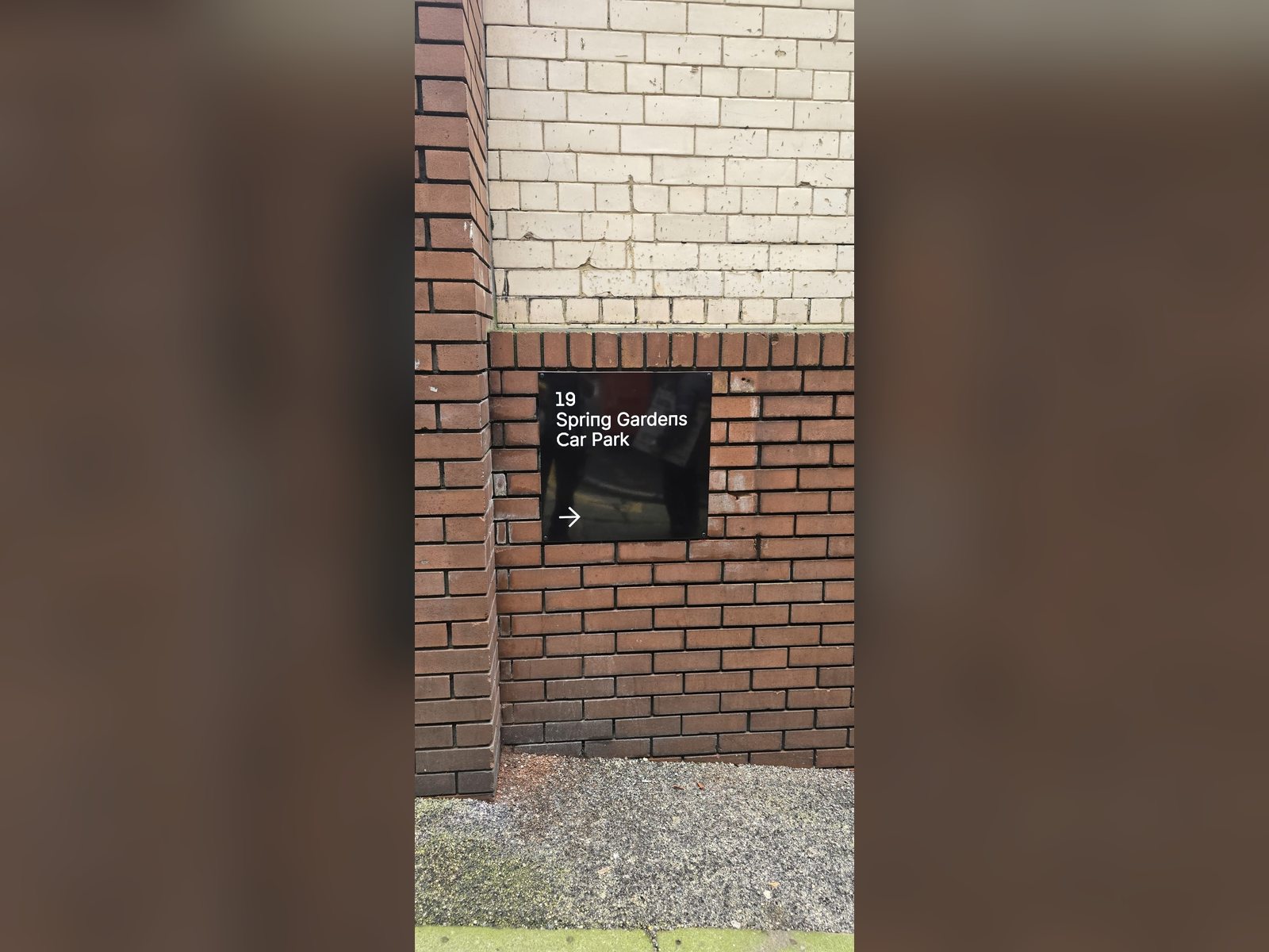 Directional car park sign with raised lettering on a brick wall