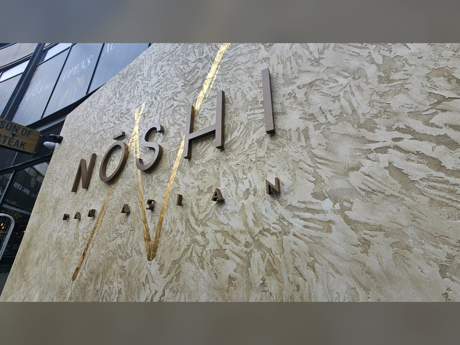 Brushed metal letters with a gold leaf N applied to a textured restaurant wall