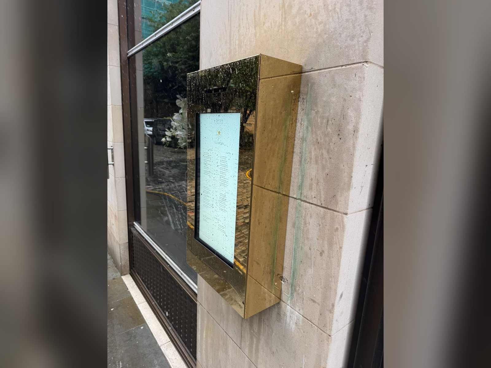Brass finish menu display case on a stone facade