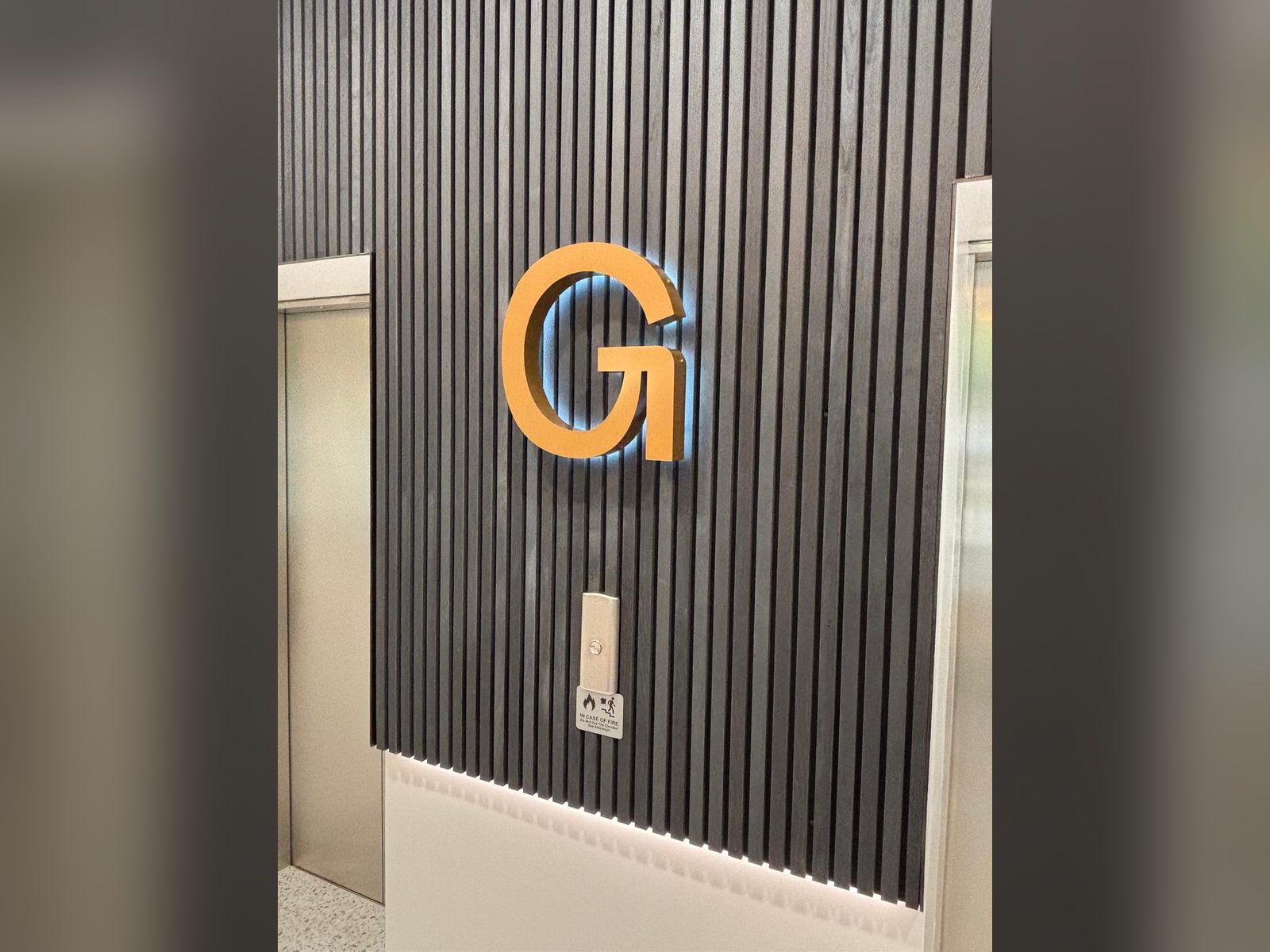 Halo lit logo letter on a dark slatted feature wall